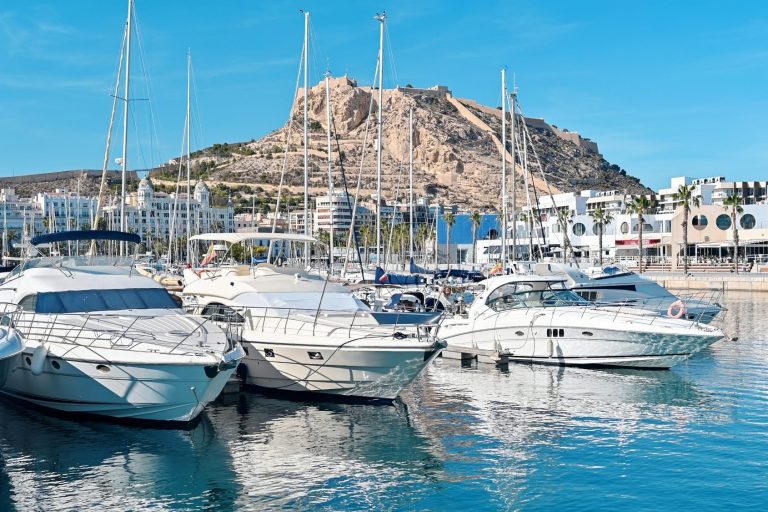 Book a massage at home with SENSE8 Sailboats lined up in Puerto Banús, with a mountain in the background and a blue sky. Book your perfect in-home massage with SENSE8